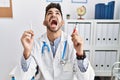 Young doctor man holding electronic cigarette at medical clinic angry and mad screaming frustrated and furious, shouting with Royalty Free Stock Photo
