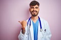 Young doctor man with tattoo wearing stethocope standing over isolated pink background smiling with happy face looking and Royalty Free Stock Photo