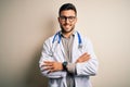 Young doctor man wearing glasses, medical white robe and stethoscope over isolated background happy face smiling with crossed arms Royalty Free Stock Photo