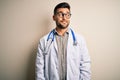 Young doctor man wearing glasses, medical white robe and stethoscope over isolated background smiling looking to the side and Royalty Free Stock Photo