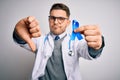 Young doctor man wearing medical coat and holding colon cancer awareness blue ribbon with angry face, negative sign showing Royalty Free Stock Photo