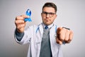 Young doctor man wearing medical coat and holding colon cancer awareness blue ribbon pointing with finger to the camera and to Royalty Free Stock Photo