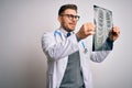 Young doctor man wearing medical coat looking at chest scan radiography over isolated background with a happy face standing and