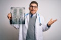 Young doctor man wearing medical coat looking at chest scan radiography over isolated background very happy and excited, winner