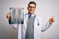 Young doctor man wearing medical coat looking at chest scan radiography over isolated background very happy pointing with hand and