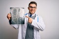 Young doctor man wearing medical coat looking at chest scan radiography over isolated background very happy pointing with hand and