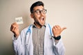 Young doctor man wearing stethoscope holding help note over isolated background pointing and showing with thumb up to the side Royalty Free Stock Photo