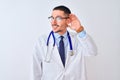 Young doctor man wearing stethoscope over isolated background smiling with hand over ear listening an hearing to rumor or gossip Royalty Free Stock Photo