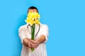 A young doctor men holds a bouquet of yellow narcissists and stands on a blue background. Concept is Mother\'s Day, March 8,