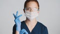 Young doctor in protective eyeglasses and medical mask wearing gloves on camera isolated. Safety concept