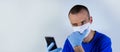 Young doctor in a protective mask and blue clothes on a blue background. looking at a mobile phone in his hand.copyspace for text