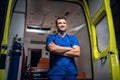 Young doctor standing and smiling in front of an an ambulance car