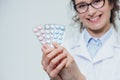 A young doctor doctor stands on a gray background isolated. During this, it holds three blister packs in its hands