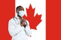 Young doctor with stethoscope and face mask praying for God with Canada national flag on background