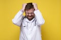 Young doctor is under stress, he is very tired, holds hair with hands and closes eyes. Psychological concept. Yellow Royalty Free Stock Photo