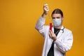 Young doctor using a pipette and a red tube, wearing protection mask and a stethoscope is trying to find a vaccine