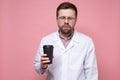 Doctor in a white coat and glasses is very tired and looks sleepy, he holds a paper cup of coffee in hands and stands Royalty Free Stock Photo