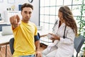 Young doctor woman checking blood pressure on patient pointing with finger to the camera and to you, confident gesture looking