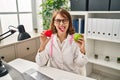 Young doctor woman holding heart and green apple sticking tongue out happy with funny expression Royalty Free Stock Photo