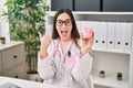 Young doctor woman holding piggy bank pointing thumb up to the side smiling happy with open mouth Royalty Free Stock Photo