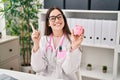 Young doctor woman holding piggy bank smiling happy pointing with hand and finger to the side Royalty Free Stock Photo