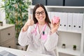 Young doctor woman holding piggy bank smiling happy and positive, thumb up doing excellent and approval sign Royalty Free Stock Photo