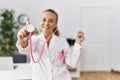 Young doctor woman holding sthetoscope close to the camera smiling happy pointing with hand and finger to the side Royalty Free Stock Photo