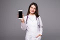 Young doctor woman pointing on cellphone screen on grey background