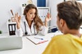 Young doctor woman showing electronic cigarette and normal cigarrete to patient in shock face, looking skeptical and sarcastic,