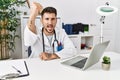 Young doctor working at the clinic using computer laptop angry and mad raising fist frustrated and furious while shouting with Royalty Free Stock Photo