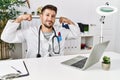 Young doctor working at the clinic using computer laptop showing arms muscles smiling proud Royalty Free Stock Photo