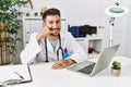 Young doctor working at the clinic using computer laptop smiling doing phone gesture with hand and fingers like talking on the Royalty Free Stock Photo
