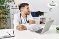 Young doctor working at the clinic using computer laptop smiling looking to the side and staring away thinking Royalty Free Stock Photo