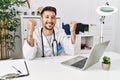 Young doctor working at the clinic using computer laptop very happy and excited doing winner gesture with arms raised, smiling and Royalty Free Stock Photo