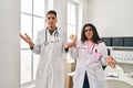 Young doctors wearing uniform and stethoscope at the clinic shouting and screaming loud to side with hand on mouth