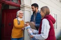 Young door to door fundraisers talking to senior woman and collecting money for charity in street.