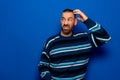 Young doubtful man thinking, scratching his head trying to find solution, isolated on blue background. Royalty Free Stock Photo