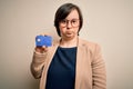 Young down syndrome business woman holding credit card as customer payment with a confident expression on smart face thinking Royalty Free Stock Photo