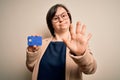 Young down syndrome business woman holding credit card as customer payment with open hand doing stop sign with serious and