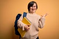 Young down syndrome student woman wearing glasses and school back holding books from library very happy and excited, winner