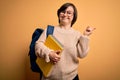 Young down syndrome student woman wearing glasses and school back holding books from library very happy pointing with hand and