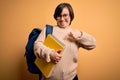 Young down syndrome student woman wearing glasses and school back holding books from library very happy pointing with hand and