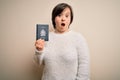 Young down syndrome tourist woman holding canada passport as trip document scared in shock with a surprise face, afraid and