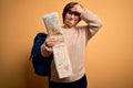 Young down syndrome tourist woman wearing bag and looking at destination city map stressed with hand on head, shocked with shame