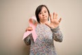 Young down syndrome woman holding breast cancer awareness pink ribbon with open hand doing stop sign with serious and confident Royalty Free Stock Photo