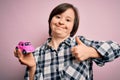 Young down syndrome woman holding small car as driving license insurance over pink background happy with big smile doing ok sign, Royalty Free Stock Photo