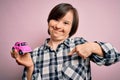 Young down syndrome woman holding small car as driving license insurance over pink background with surprise face pointing finger Royalty Free Stock Photo