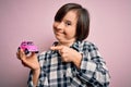 Young down syndrome woman holding small car as driving license insurance over pink background very happy pointing with hand and Royalty Free Stock Photo