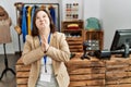 Young down syndrome woman working as manager at retail boutique begging and praying with hands together with hope expression on