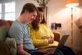 Young Downs Syndrome Couple Sitting On Sofa Using Laptop At Home